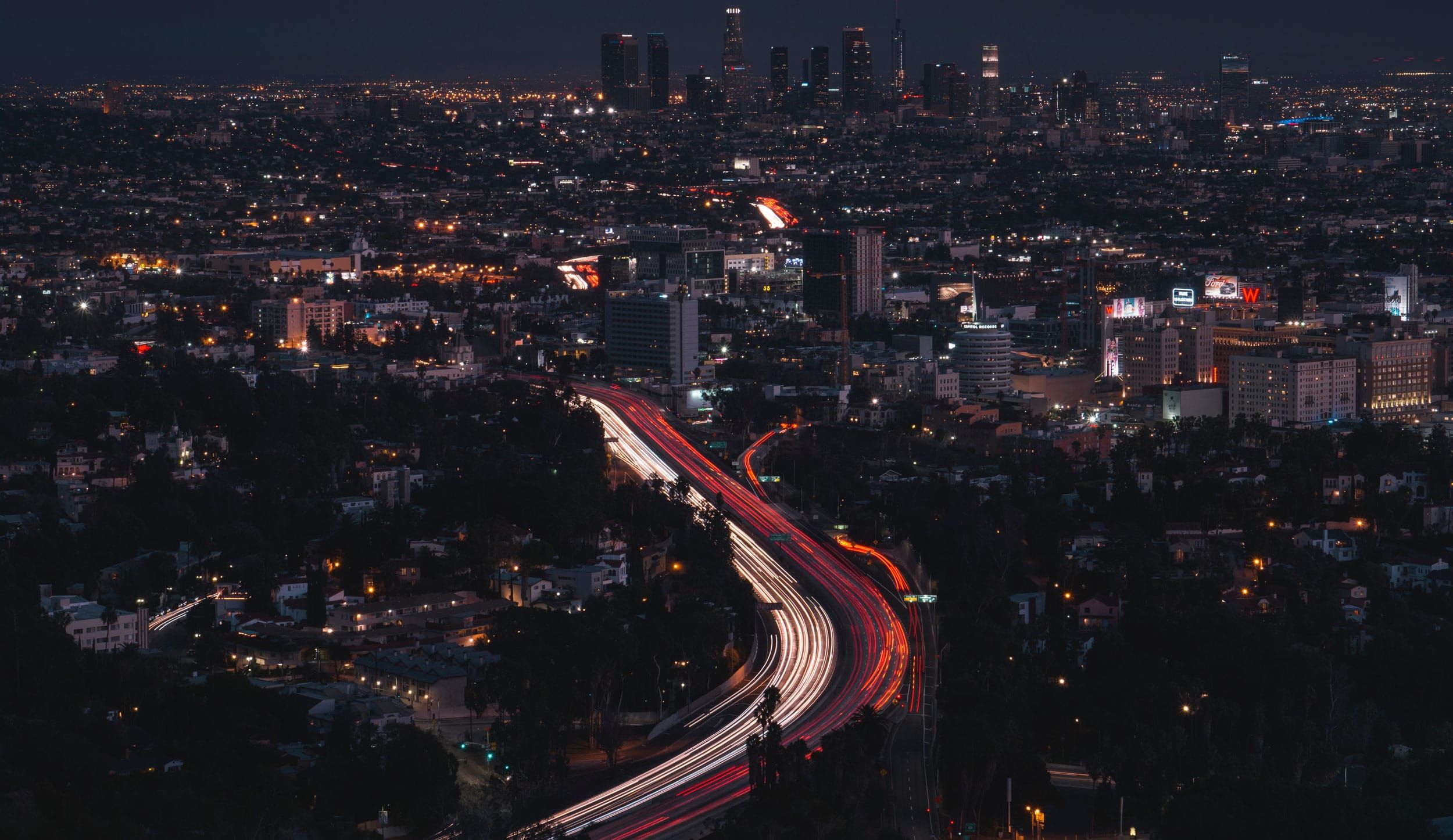 Los Angeles skyline at night, showing lights of cars traveling along the freeway.
